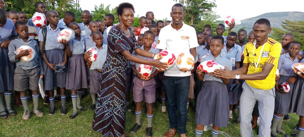 Fortebet's John Nanyumba (in white) handing over the balls to the headmistress, Christine Alinaitwe together with gamesmater and pupils